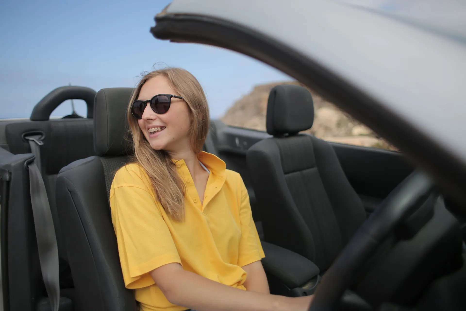 Emma met zonnebril, lachend in een open auto