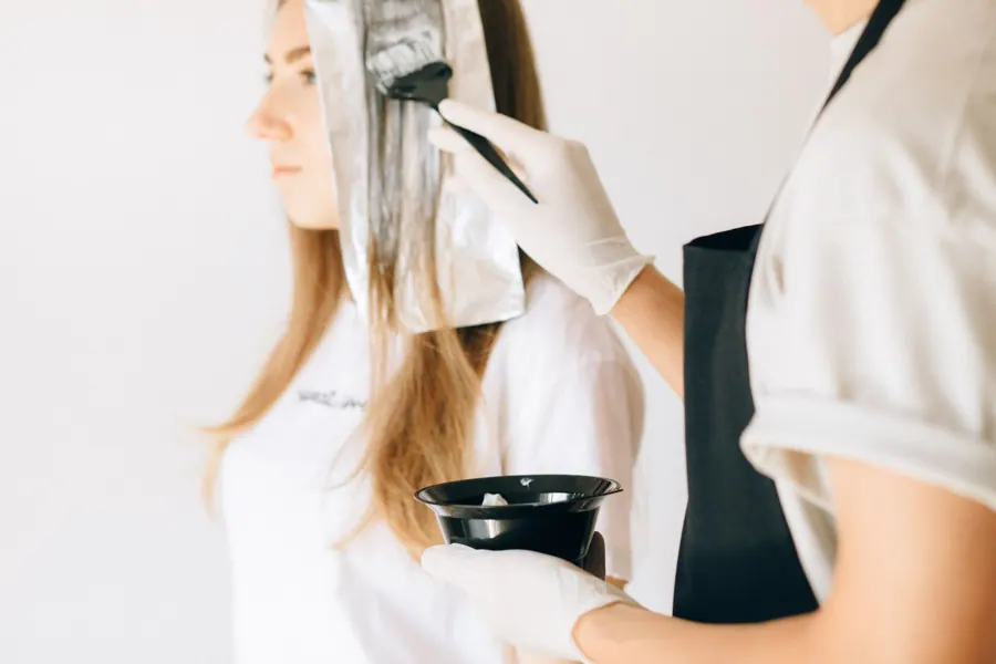 Een kapster brengt met een kwast kleur aan in lang blond haar