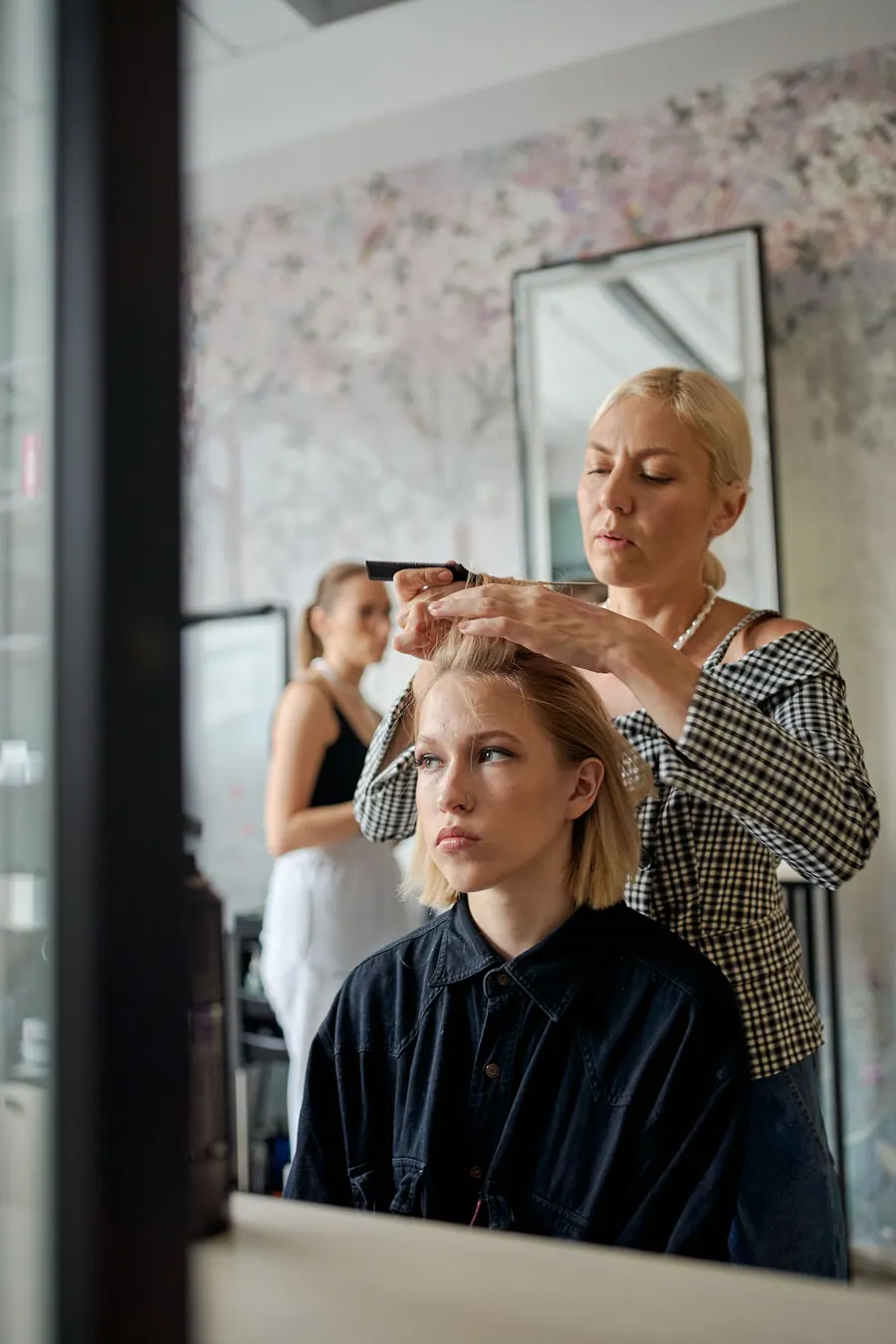 Een kapster knipt een klant met kort blond haar voor een grote spiegel