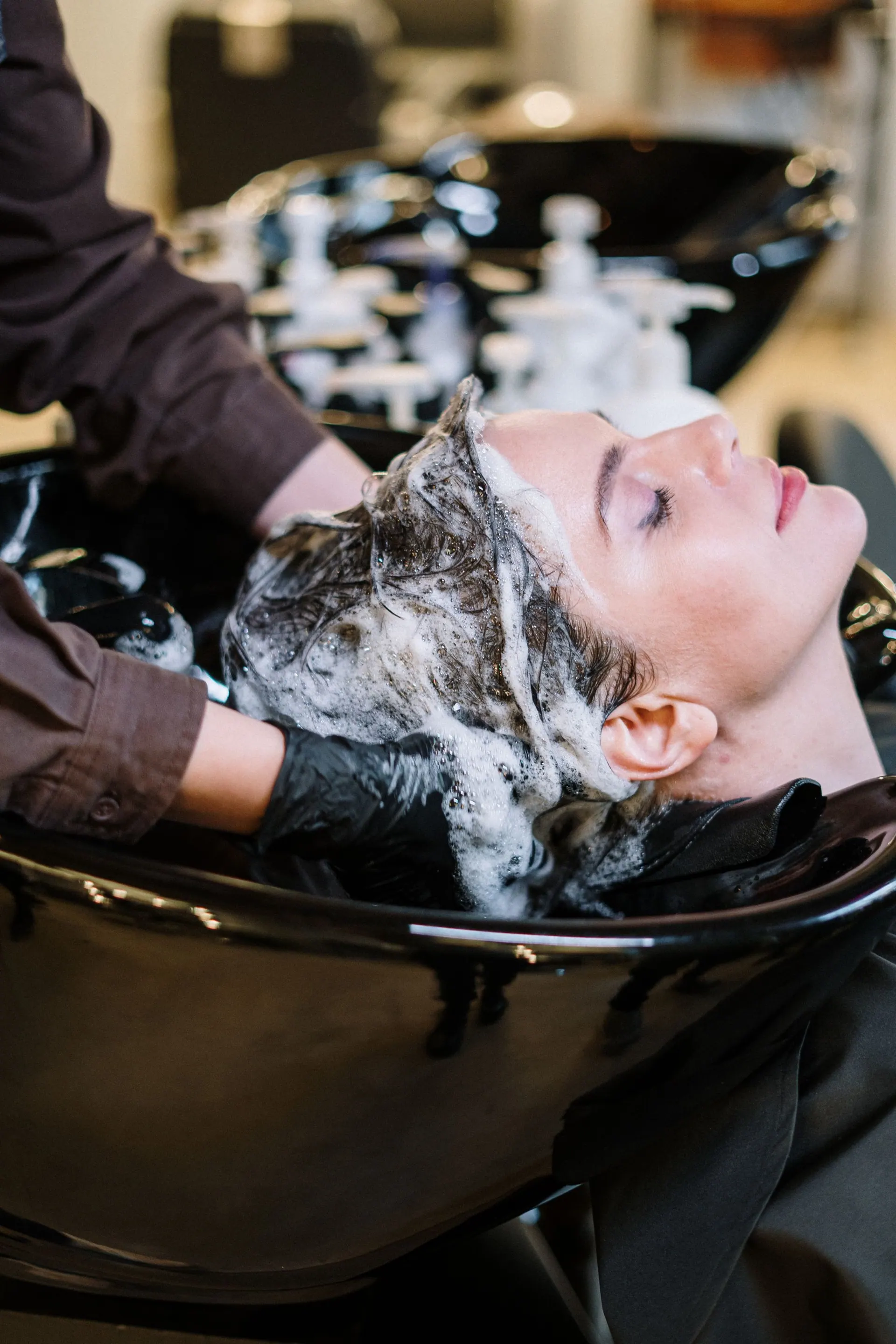 Een klant ontspant met shampoo in het haar bij de wasbak