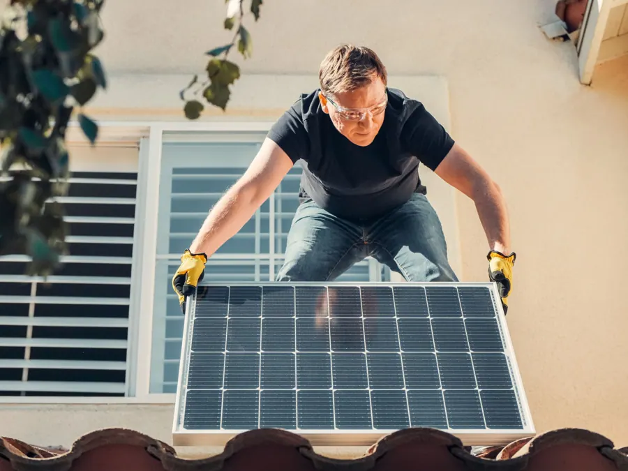 Monteur tilt een zonnepaneel over de dakrand van een woning