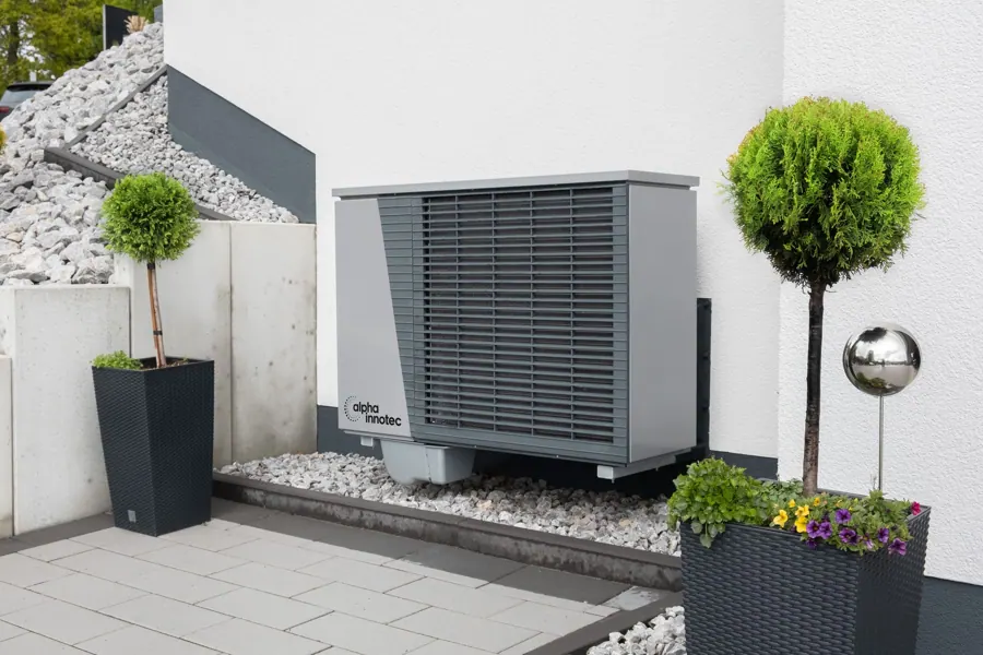 Warmtepomp op een grindbed naast de gevel met potten buxus