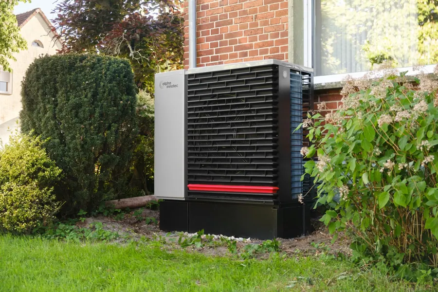 Buitenunit van de hybride warmtepomp tussen de struiken in de achtertuin