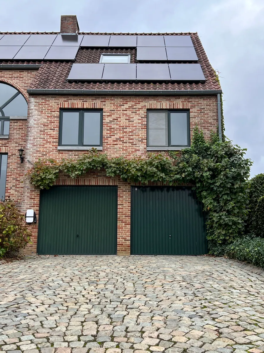 Bakstenen huis met zonnepanelen op het dak en groene garagedeuren