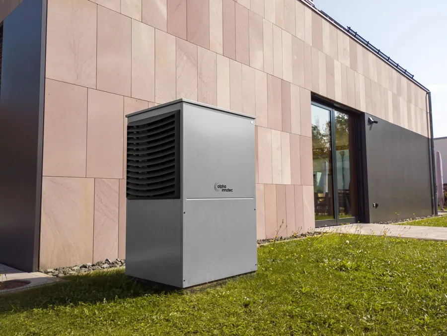 Grijze warmtepomp op het gras naast een moderne gevel